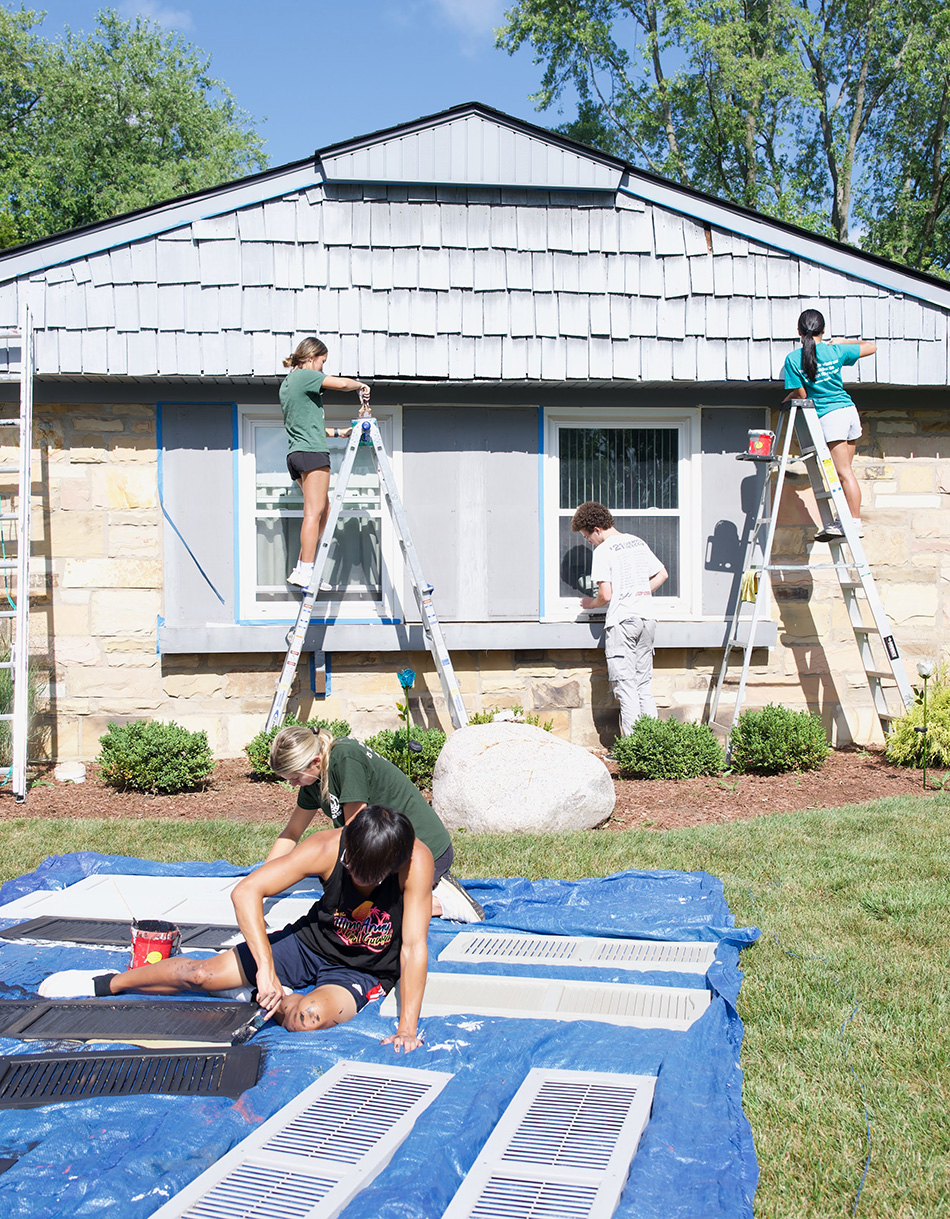 Two teenage girls painting peak of house on ladders